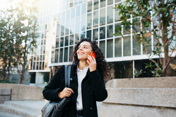 Fototapeta premium Young businesswoman talking on a red smartphone on the street