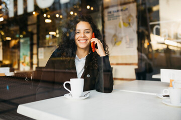 Young woman talking on a red smartphone  and drinking coffee in a coffeeshop