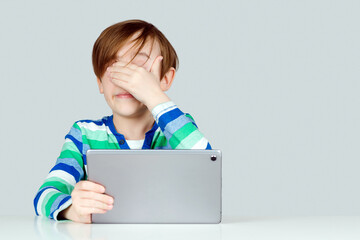 Tired little student feeling eyestrain during online lesson. Kid rubbing dry irritated eyes, sitting at desk with pc.