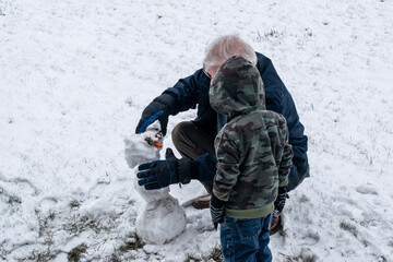 Boy with grandpa building small snowman in winter