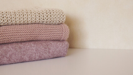 Fototapeta na wymiar A stack of knitted things on a light background. Folded knitted clothes in pink and beige colors. Housekeeping concept.