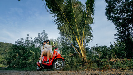 Scooter road trip. Love couple on red motorbike in white clothes on forest road trail. Just married woman and man kiss, hugs, sit on motorbike. Wedding, honeymoon. Motorcycle rent. Safety helmet.