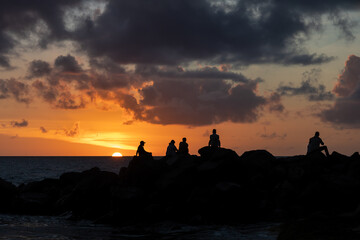 Key West, Florida, USA - December 2021 - Group of people watching a colorful sunset, only silhouettes visible against the sun.