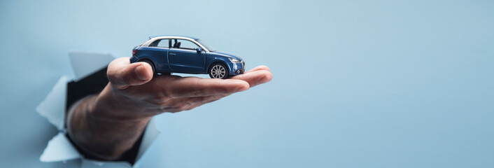 Man's hand holding a car on a blue background - obrazy, fototapety, plakaty