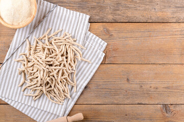 Whole grain wheat raw apulian pasta Pizzarieddi or maccaruni on a napkin board on wooden table. Fresh maccheroni typical dish of Puglia Salento Italy. Italian homemade pasta background, top view