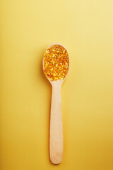 Vitamin D3 Capsules in a spoon with other vitamin D3 capsules around them on a yellow background