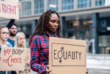 Young African woman leading a group of demonstrators in city streets, multiracial people protesting for equality and empowerment, feminism protest