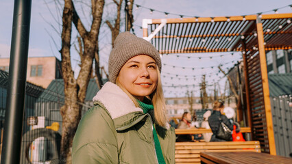 Fototapeta na wymiar Smiling blonde woman sitting at a table in an urban space street cafe with street food. Warm winter day to meet friends