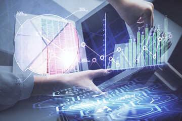 Double exposure of businesswoman hands typing on computer and financial graph hologram drawing....