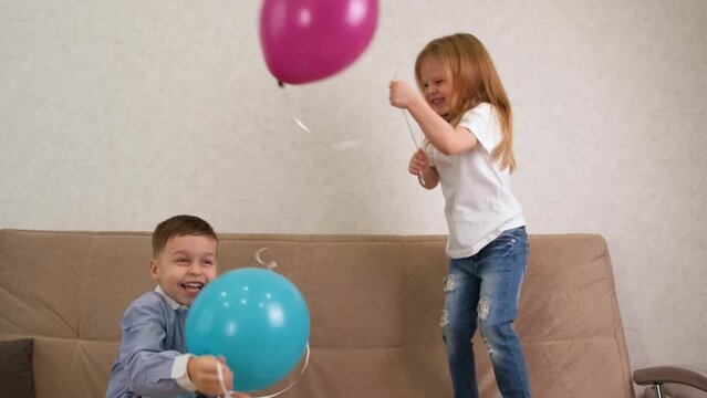 A little girl and a boy jump on the sofa with balloons and have fun. Children celebrate the holiday. Birthday concept