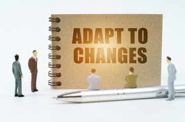 On a white background, figures of businessmen, a pen and a notepad with the inscription - Adapt to...