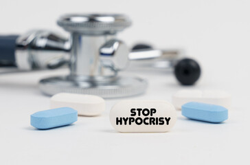Obraz na płótnie Canvas On a white surface lie pills, a stethoscope and a tablet with the inscription - STOP HYPOCRISY