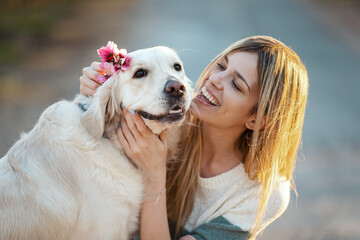 Beautiful woman stroking and pampering her lovely golden retriever dog while he putting a flower on her head sitting on the floor in a cherry field in springtime.