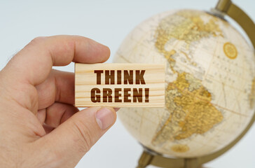 A man holds in his hand a wooden plate on which it is written - Think Green. In the background is a globe.