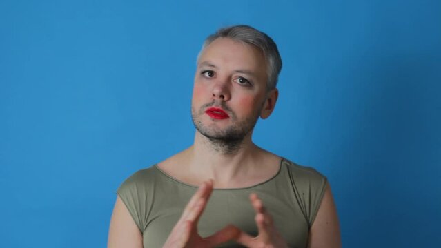 A gay man with makeup on his face on an isolated blue background is a transsexual LGBT blogger.