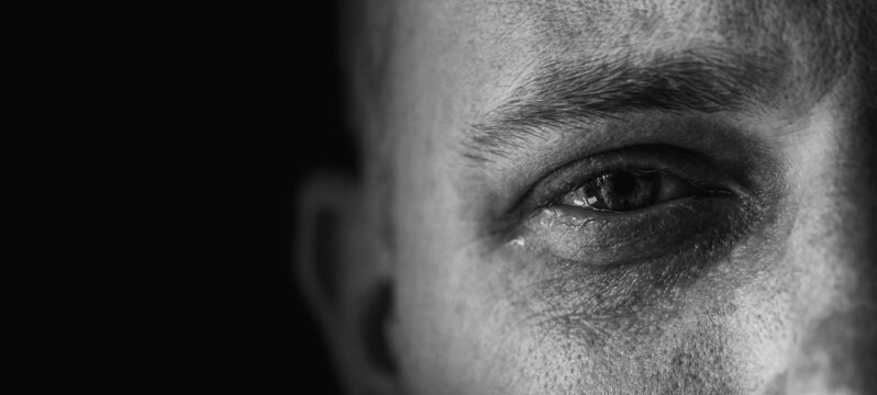 Dunkle Aufnahme eines traurigen Mannes mit einem weinenden Auge im Detail