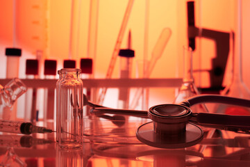 Stethoscope among chemical glassware on a desk - labs photo. Red and orange color hues of...