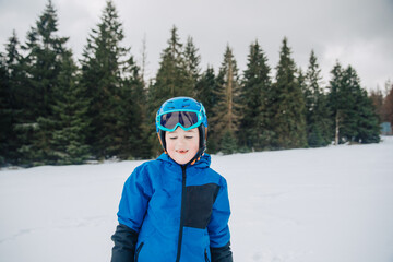 Fototapeta na wymiar portrait of a child in a helmet and ski goggles. Little boy on the slope. Child with ski equipment smiles and has fun on the slope. Child in ski school learns to ski