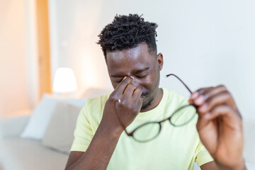 African man in glasses rubs his eyes, suffering from tired eyes, ocular diseases concept