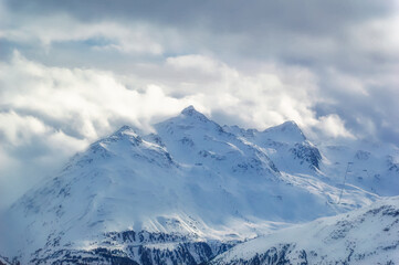 Snow covered Alps peak with cloudy sky background during winter day.