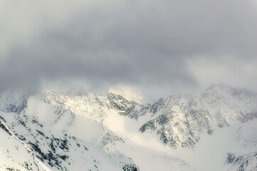 Snow covered Alps peak with cloudy sky background during winter day.