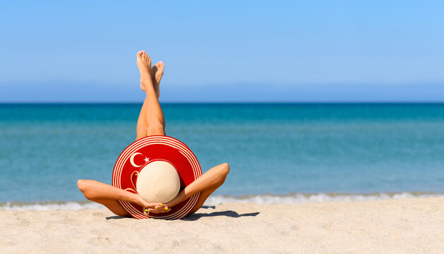 A slender tanned girl on the beach in a straw hat in the colors of the flag of Turkey. The concept of a perfect vacation in a resort in the Turkey. Focus on the hat.