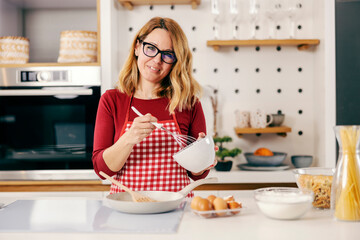 A happy housewife making meal in kitchen at her comfortable home.