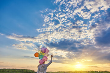 Girl with balloons running on the field to the sun