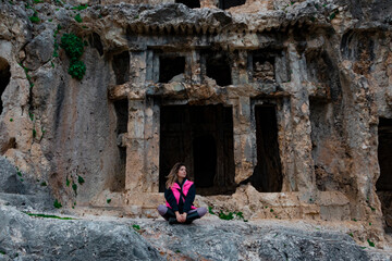 Tlos ancient city from Fethiye, Turkey. Young girl is sitting on rocks. She is looking side. She wears pink winter clothes.	
