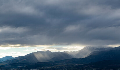 Fototapeta na wymiar Sun ligths coming between clouds to snowy mountain. A sharp light seems on the photo. Amazing view.
