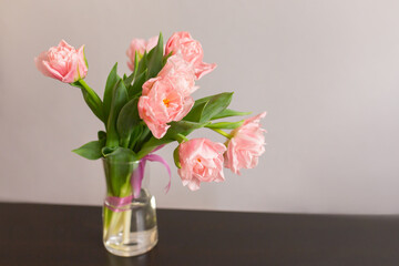 Pink tulips with green leaves in a glass vase on the table. Place for text