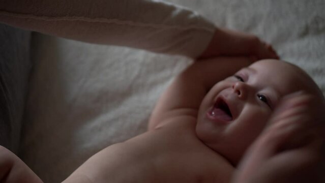 Newborn Baby And Young Mom Lie On Bed. Cute Smiling Teethless Kid Face Portrait. Woman Makes Massage Naked Child. Mother Care Of Babe. Infant, Mother Day, Childbirth, Beginning, Relationship Concept