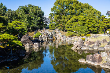Fototapeta na wymiar Japanese Garden with a shallow pond and rocks surrounding the edge in daylight.