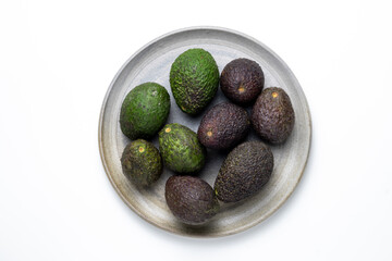 Avocados in different rippening stageson a ceramic plate in cenital frame 