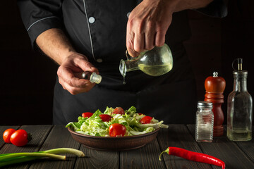 The chef pours olive oil into a bowl of salad. Cooking tasty and healthy food with set of vitamins
