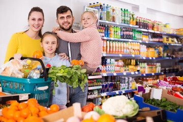 Obraz premium Two small positive sisters during family shopping in greengrocery department of supermarket