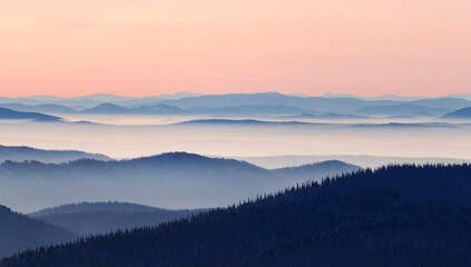 Naklejka na ściany i meble Mountain range with visible silhouettes through the morning colorful fog. Beautiful mountain background.