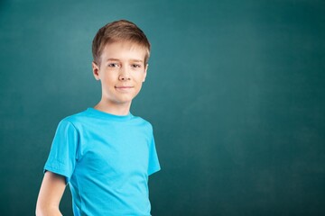 Happy cute kid boy school student looking at camera at blackboard background.