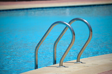 Close up of swimming pool stainless steel handrail descending into tortoise clear pool water. Accessibility of recreational activities concept