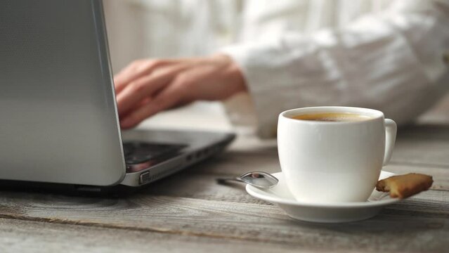 Protable coffee hand computer. A working girl at a laptop computer and drinks black coffee with foam. White cup of coffee
