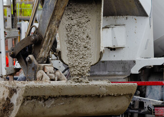 Excavator bucket filled with wet concrete to bring it to place of concrete works on building site