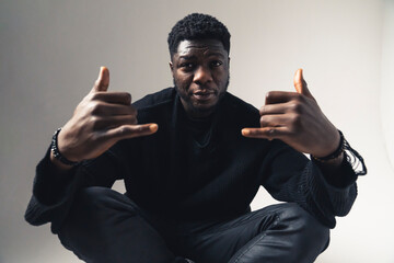 Afroamerican men with shaka sign seated chill white background - mid-full shot. High-quality photo