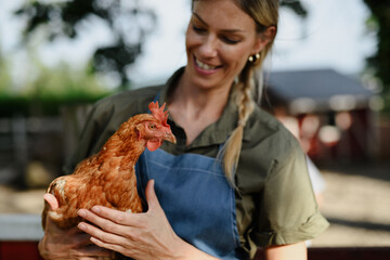 Cheerful farmer woman holding hen outdoors at farm.
