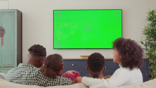 Rear view of family sitting on sofa at home watching green screen TV and laughing at comedy - shot in slow motion