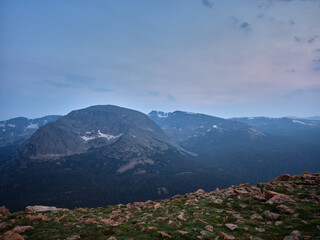 Fototapeta premium Glacial Leftover granite boulders lead down into a deep glacial created valley with mountain peaks in the background in the Rocky Mountains