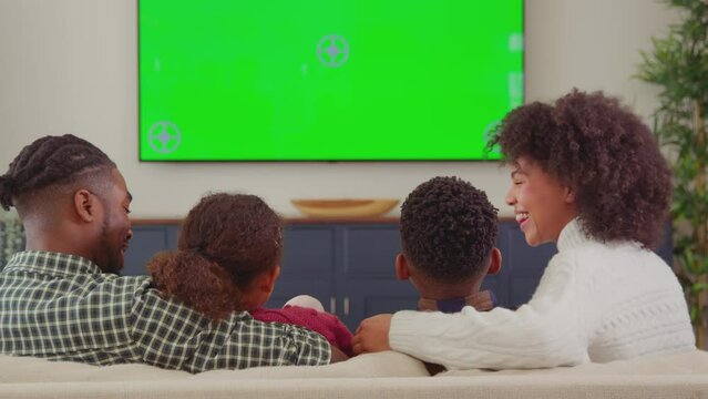Rear view of family sitting on sofa at home watching green screen TV and laughing at comedy - shot in slow motion