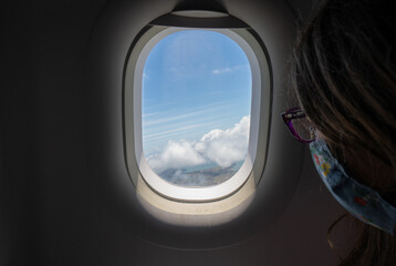 Young Girl Looking Out Airplane Window Over Ocean and Clouds on a Sunny Day at Take Off