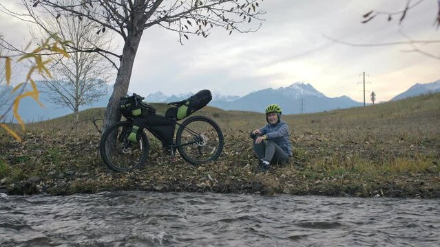 The woman travel on mixed terrain cycle touring with bikepacking. The traveler journey with bicycle bags. Sportswear in green black colors. The trip in magical autumn forest, river stream.