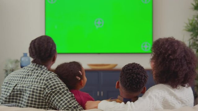 Rear view of family sitting on sofa at home watching green screen TV and laughing at comedy - shot in slow motion