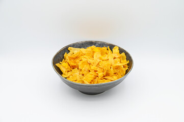 Corn Flakes, in a dark grey bowl, isolated on a white background